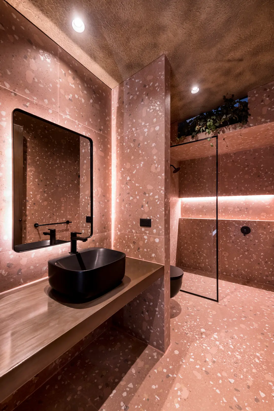 Baño revestido en tonos rojizos con iluminación indirecta