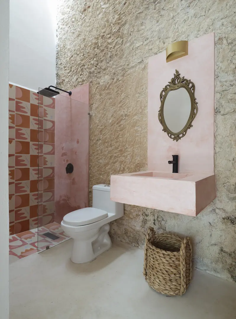 Mosaicos y piedra en uno de los baños Baño de Casa Luciérnagas con lavabo rosa, muro de piedra y mosaicos