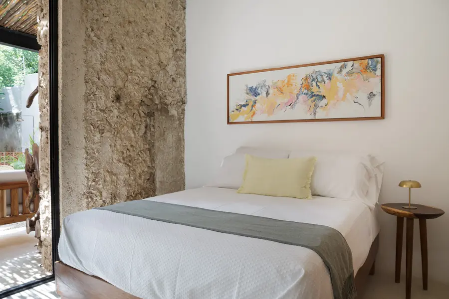 Un dormitorio de tonos naturales junto al muro original Dormitorio de Casa Luciérnagas con muro de piedra y textiles claros