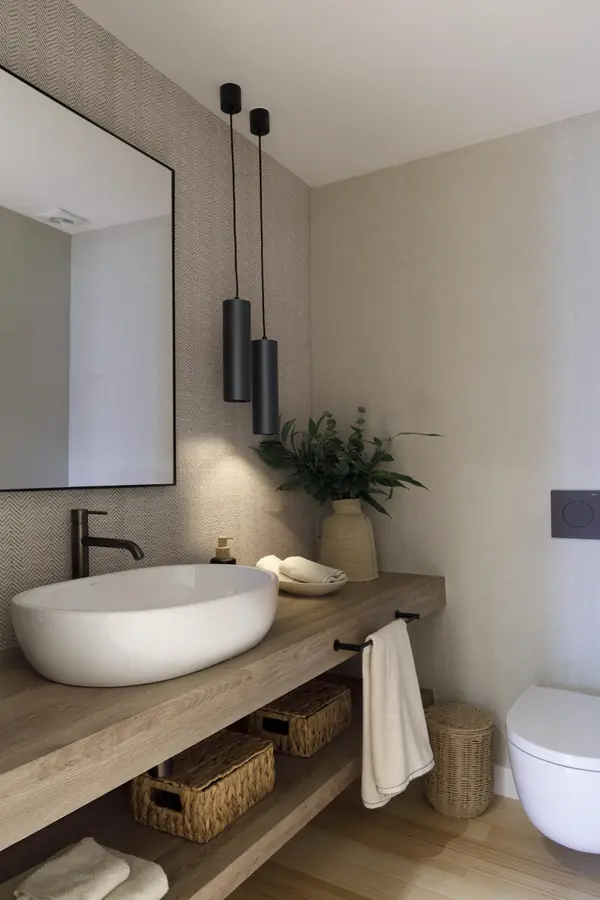 Aseo de cortesía con madera y papel pintado Aseo de cortesía con lavabo sobre encimera de madera, grifería negra y pared de papel pintado geométrico