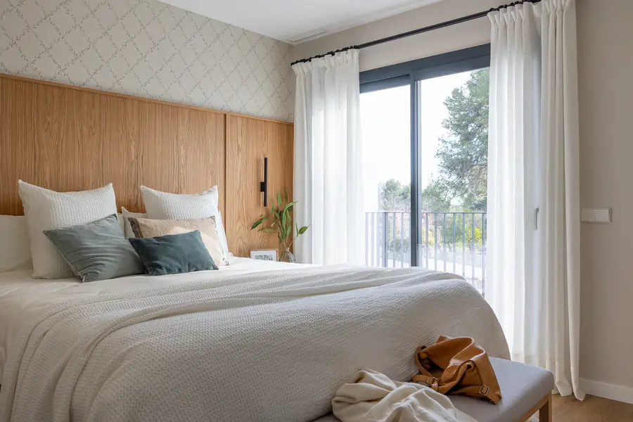 Dormitorio principal iluminado junto a un ventanal con cortinas ligeras