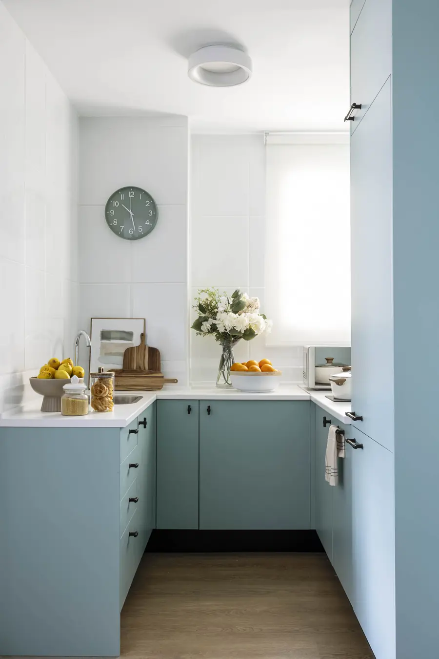 Frentes turquesa en una cocina compacta Cocina pequeña con muebles turquesa, encimera blanca y ventana al fondo
