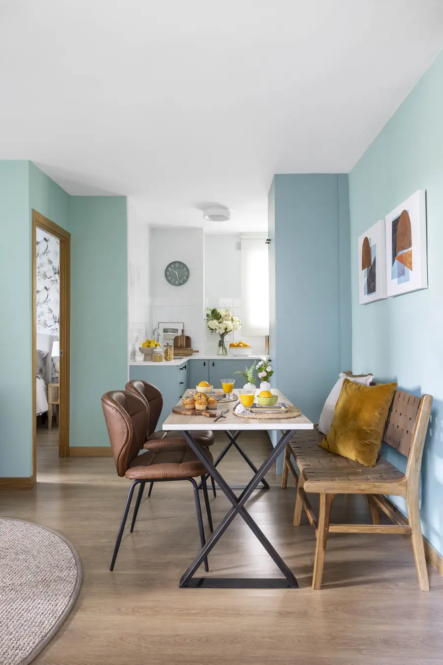 Un comedor con banco junto a la cocina Mesa rectangular con banco de madera, dos sillas y cojines mostaza junto a la cocina