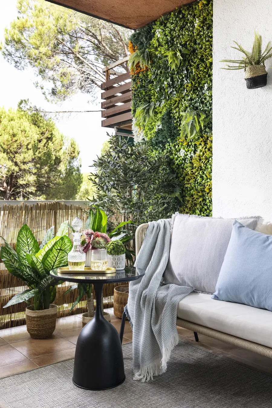 Un rincón de terraza protegido por vegetación Sofá beige de terraza junto a una pared de vegetación artificial y barandilla revestida de fibra